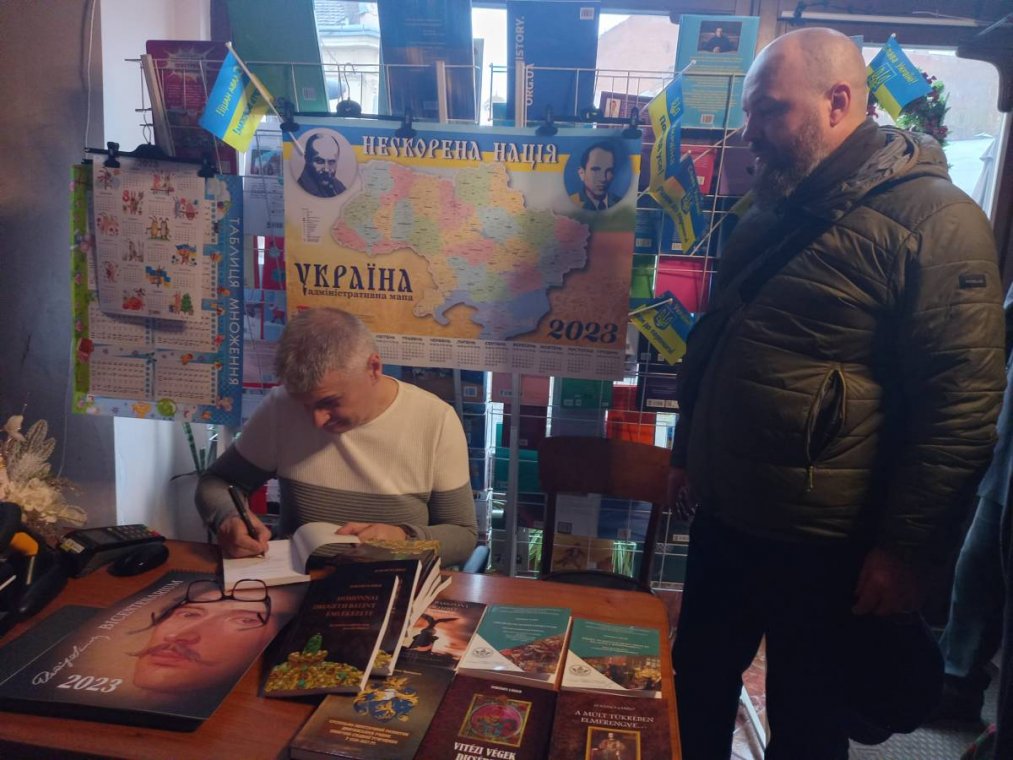Ласло Зубанич підписує книгу для закарпатців, що нині боронять нашу землю на фронті. Поруч Владислав Товтин Письменницьке чергування за прилавком «Кобзаря» з історичною розвідкою про Валентина Другета продовжив доцент УжНУ Ласло Зубанич